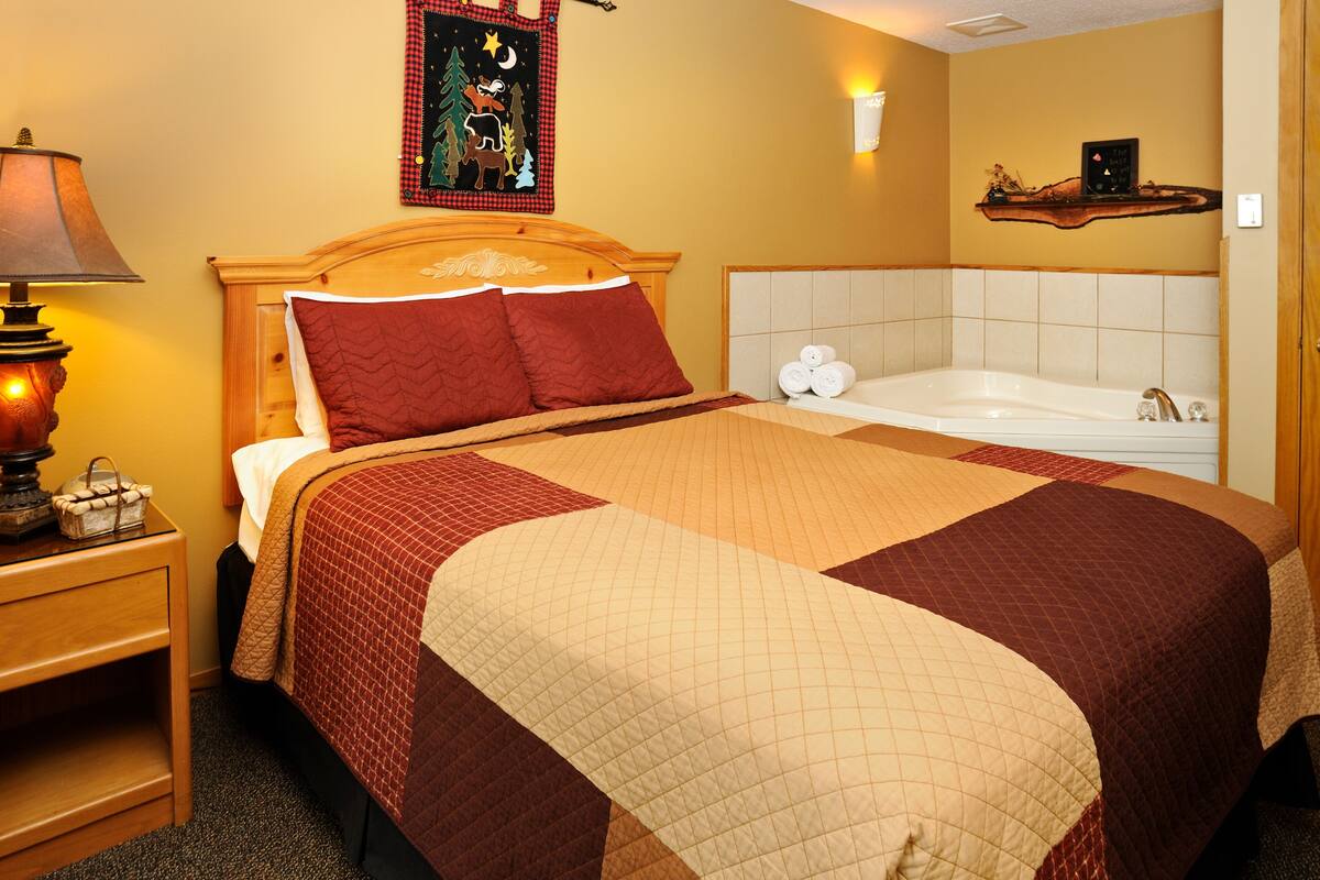 A neatly made bed with a quilt, a bedside lamp, and a nightstand with a basket.