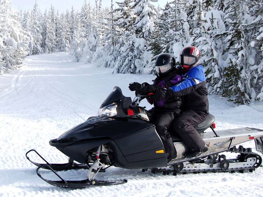 A snowmobile on a snowy path with trees on either side.