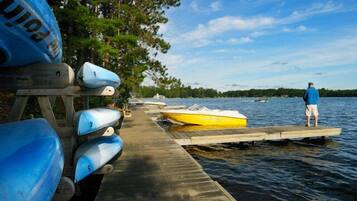 A wooden dock extending into a lake with several kayaks and a speedboat docked.