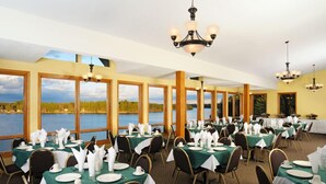 A dining area with tables set for service, large windows with a view of a lake, and chandeliers. - The Pointe Hotel and Suites (Minocqua)