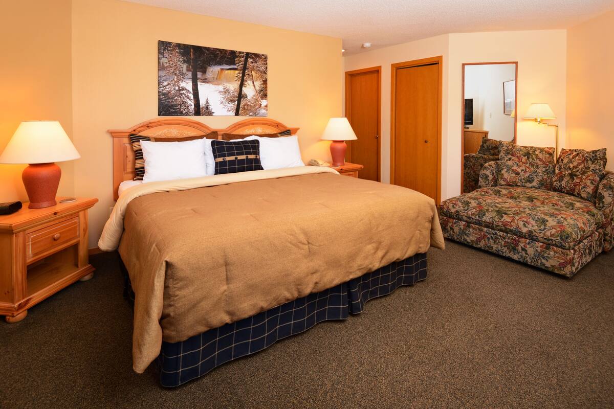 A hotel room with a large bed, two bedside tables with lamps, a floral sofa, and a painting on the wall.