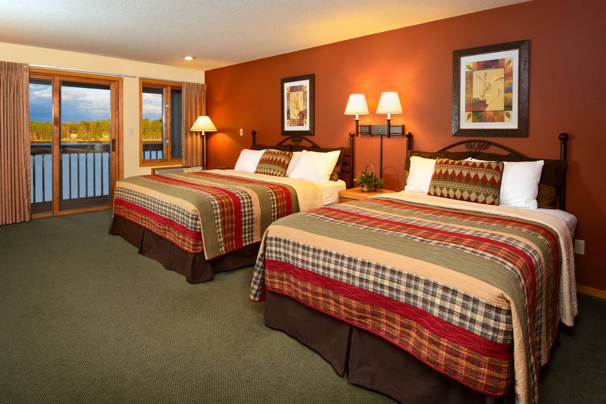 A hotel room with two beds, a balcony, and a view of the outdoors.
