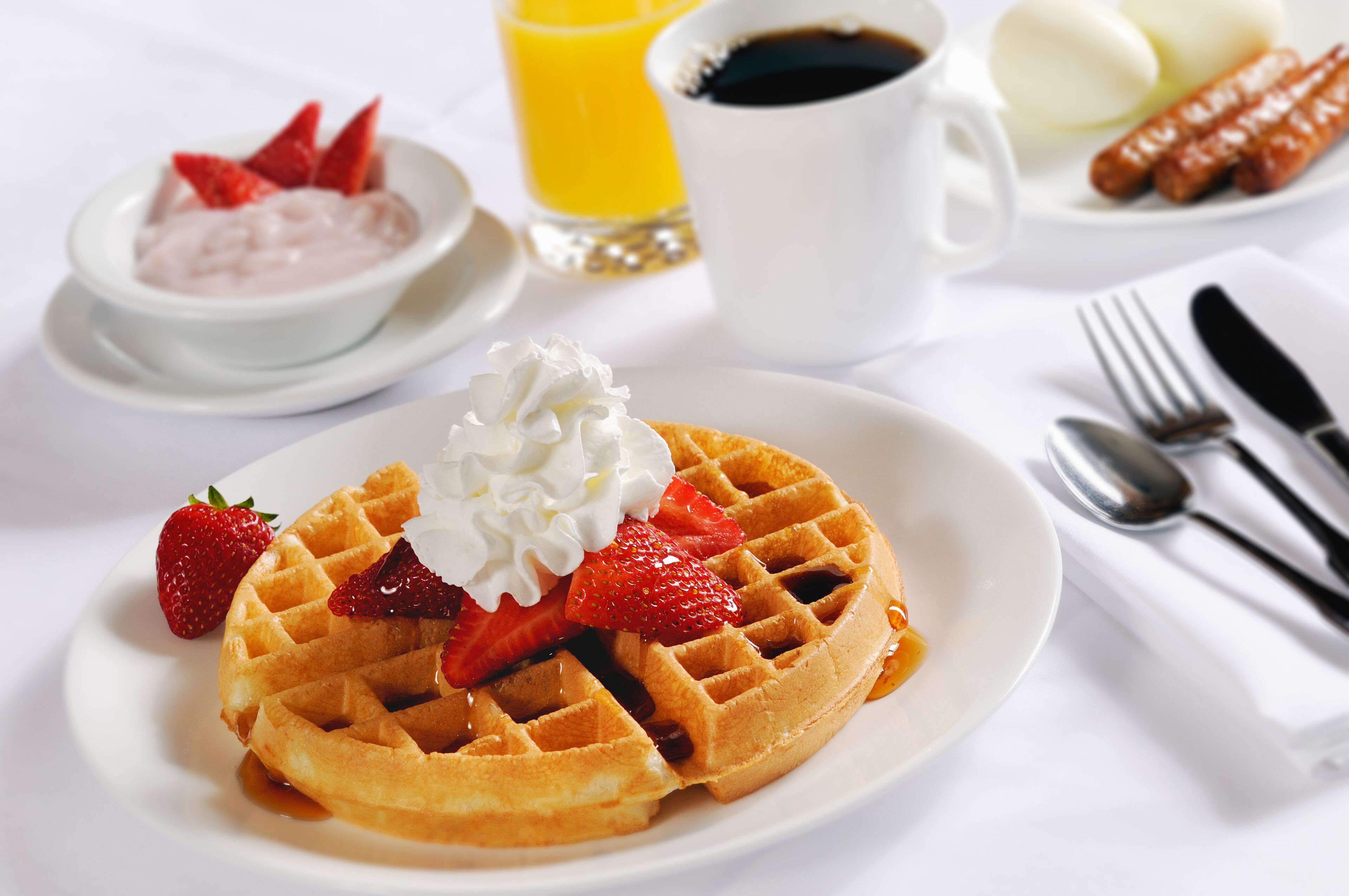 A breakfast plate with a waffle, strawberries, and whipped cream.