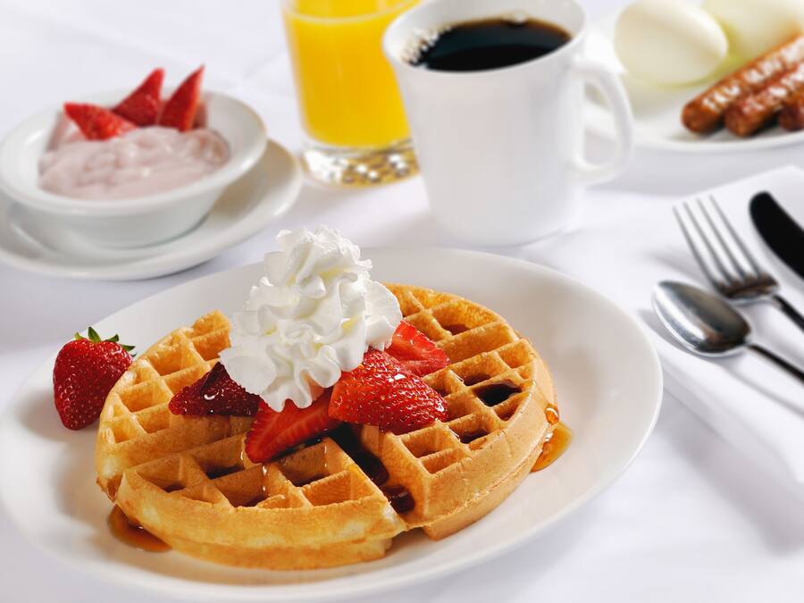 Un plato de desayuno con un gofre, fresas y crema batida.