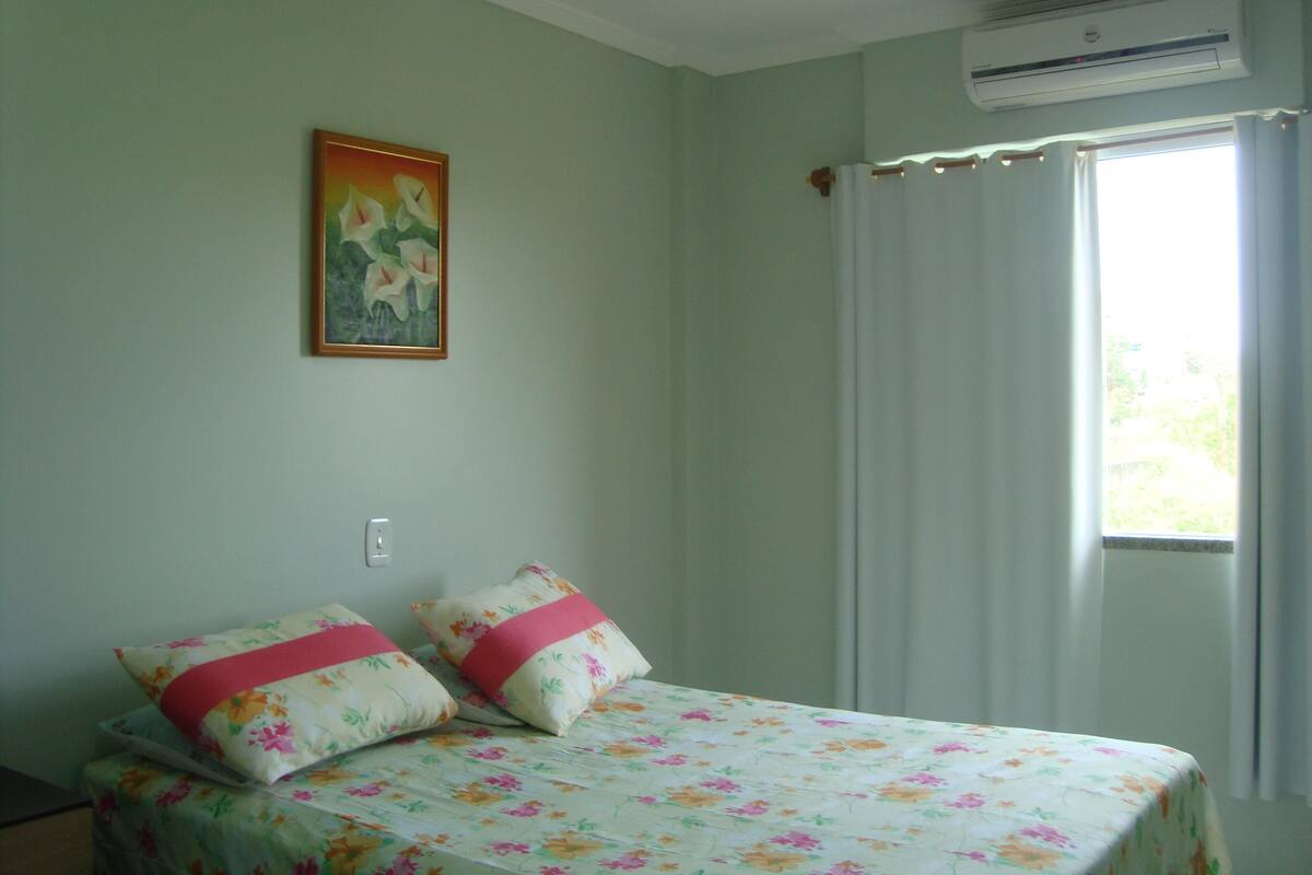 Une chambre à coucher avec un lit, un tableau, un climatiseur et une fenêtre avec des rideaux.