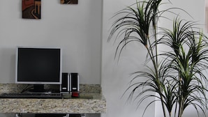 A workspace with a desktop computer, two paintings, a potted plant, and a chair. - Paradise Hotel (Campo Grande)