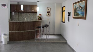 A modern kitchen with granite countertops, wooden cabinets, and a bar area with bar stools. There are two framed pictures on the wall and a telephone mounted on the wall. - Paradise Hotel (Campo Grande)