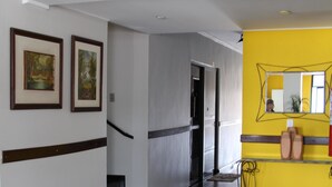 A hallway with a staircase, a yellow accent wall, and framed pictures on the left. - Paradise Hotel (Campo Grande)