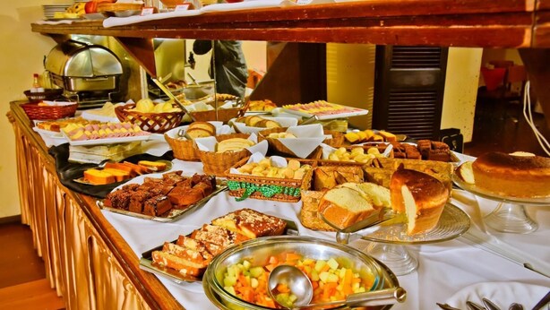 A buffet with various food items including bread, pastries, and a fruit bowl. - Hotel Estoril (Pelotas)