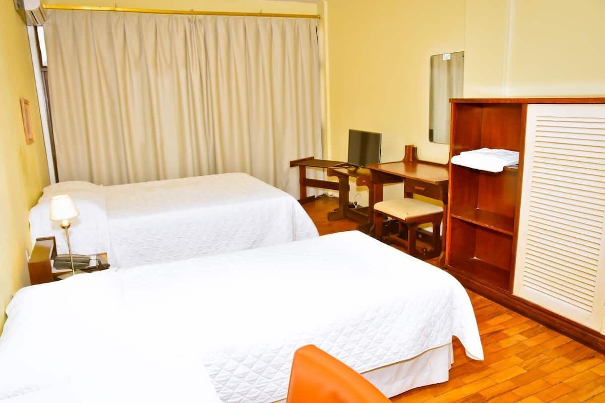 Habitación de hotel con dos camas, un escritorio, una silla, un armario y un espejo.