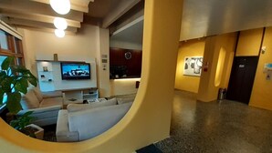 A modern lobby with a curved wall, a seating area with a television, and a reception desk. - Hotel Estoril (Pelotas)