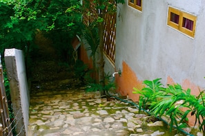 A narrow stone pathway leading to a building with a wooden gate and a small window. - Cabañas Telayú (Santa María Tonameca)