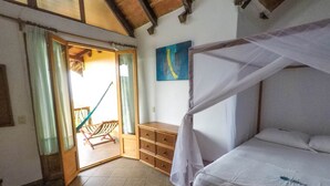 A bedroom with a bed, a wooden chest of drawers, a hammock, and a painting on the wall. - Cabañas Telayú (Santa María Tonameca)