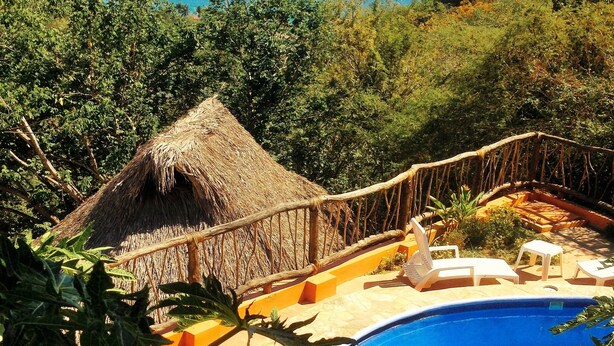 A pool area with a thatched roof structure, lounge chairs, and a view of the ocean. - Cabañas Telayú (Santa María Tonameca)