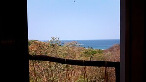 A view of the ocean through a window with a view of the beach and vegetation. - Cabañas Telayú (Santa María Tonameca)