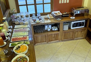 Disposição de buffet com diversos alimentos, micro-ondas e vista pela janela.