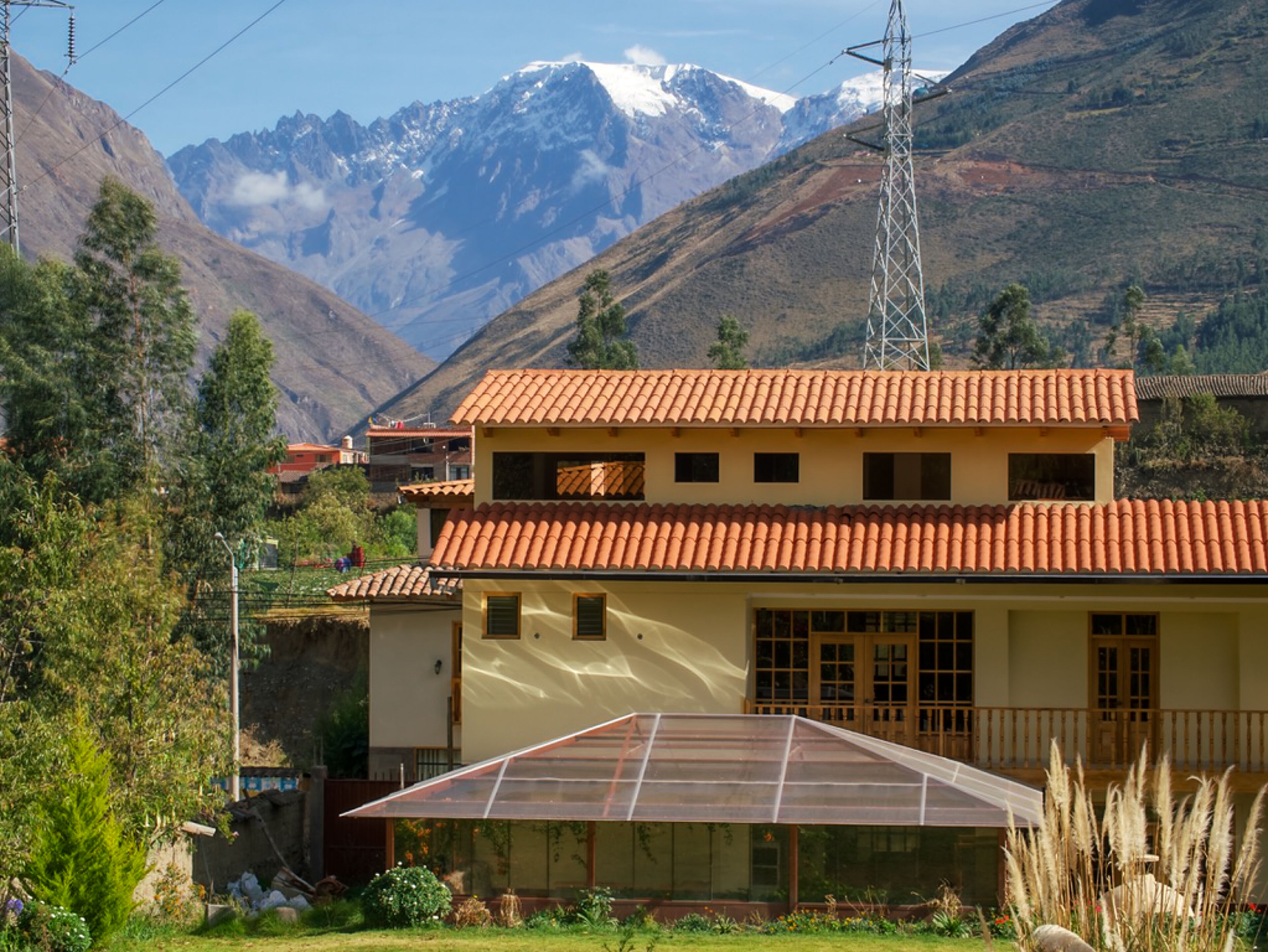 Um edifício de dois andares com telhado de telhas vermelhas, uma grande estufa de vidro e montanhas ao fundo.