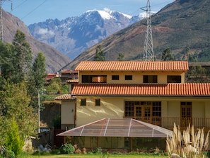 Un edificio de dos pisos con tejido rojo, un invernadero grande de vidrio y un paisaje montañoso al fondo.