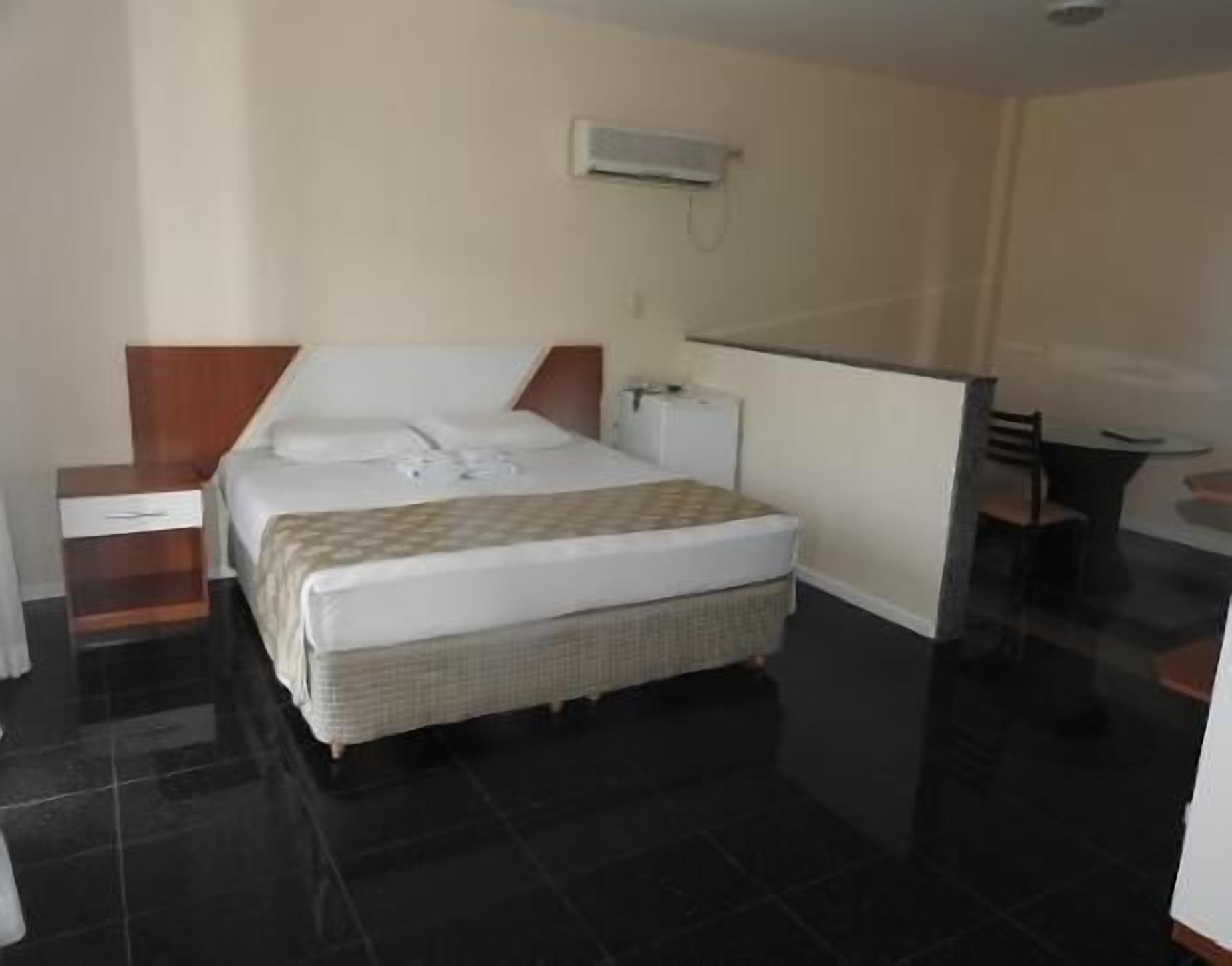 Una habitación de hotel con cama, mesita de noche, silla y una pequeña mesa.
