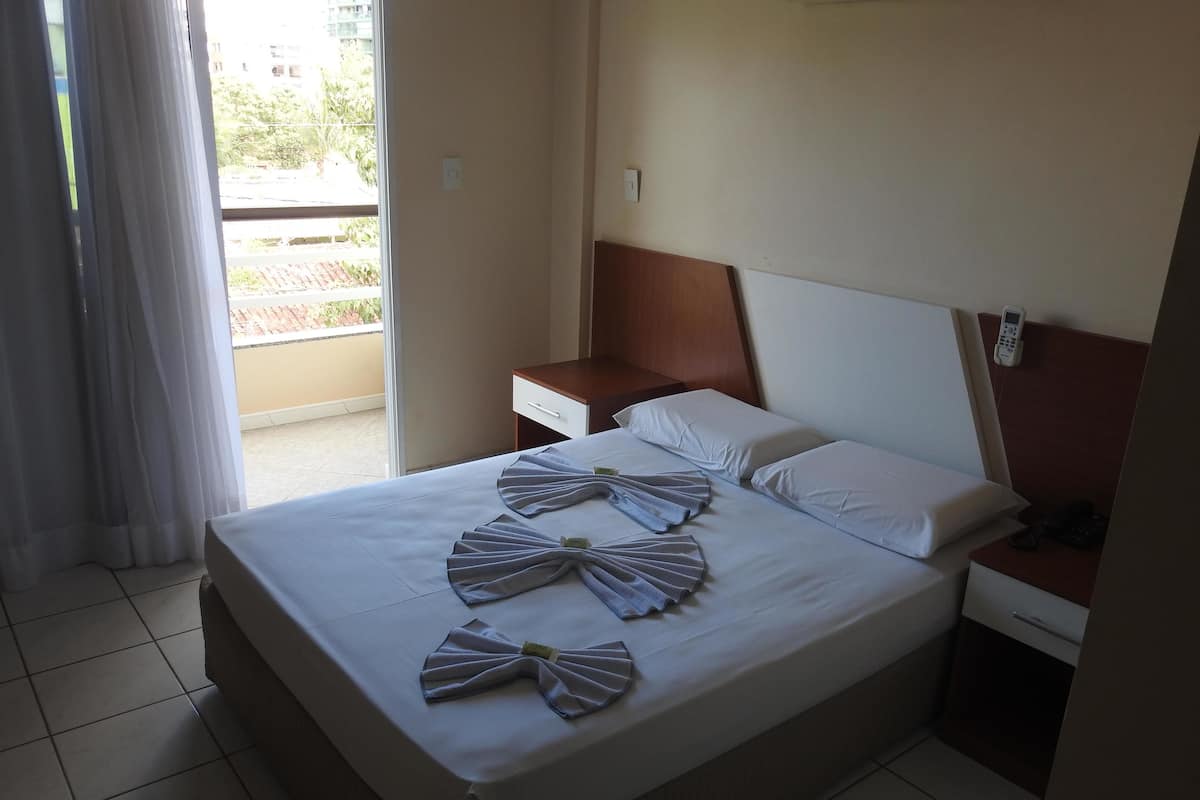 Habitación de hotel con cama, mesita de noche, teléfono y vista al balcón exterior.