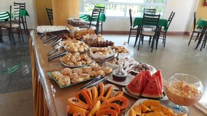 Una mesa de buffet con diversos alimentos, como frutas y pasteles, en una sala con sillas y mesas.