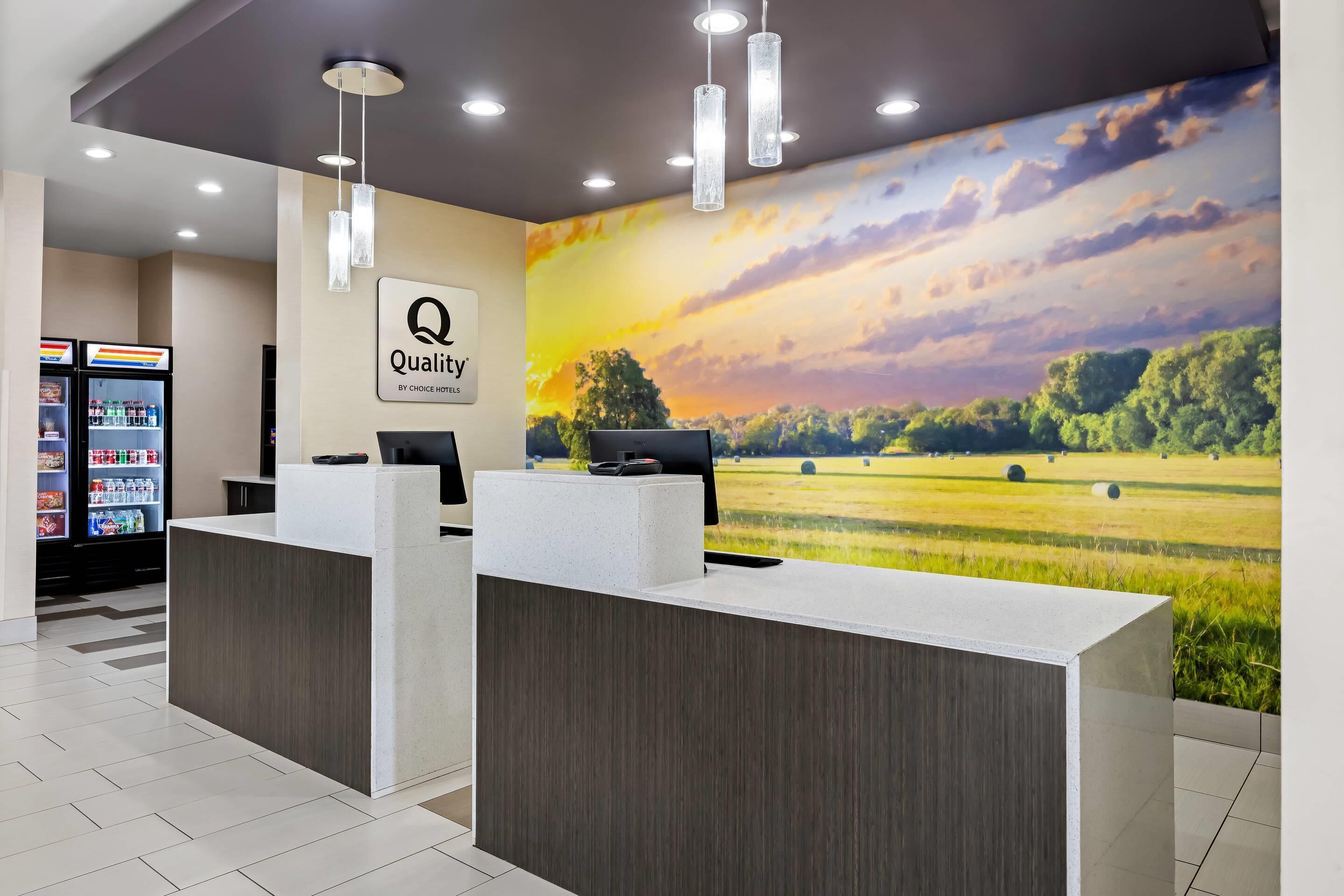 A hotel reception desk with a 'Quality by Choice Hotels' sign, a computer, and a vending machine.
