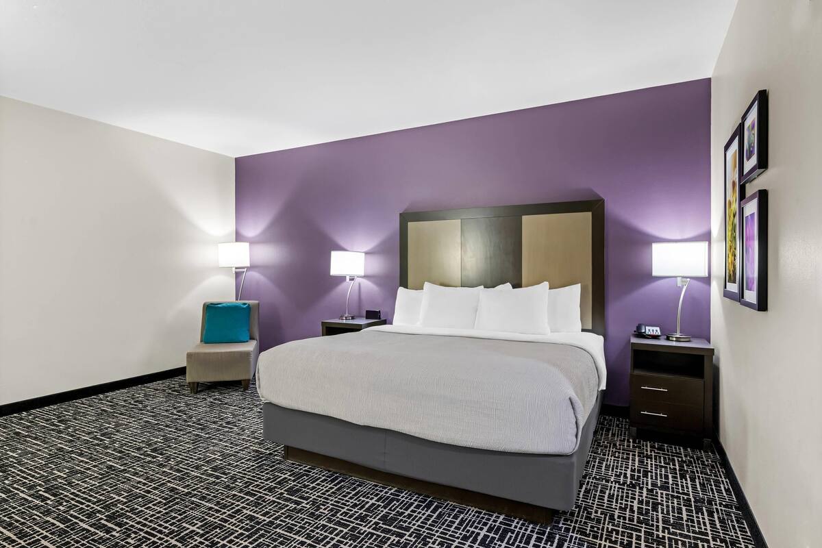 Een hotelkamer met een groot bed, twee nachtkastjes, een stoel en een kamerbreed tapijt met een patroon.