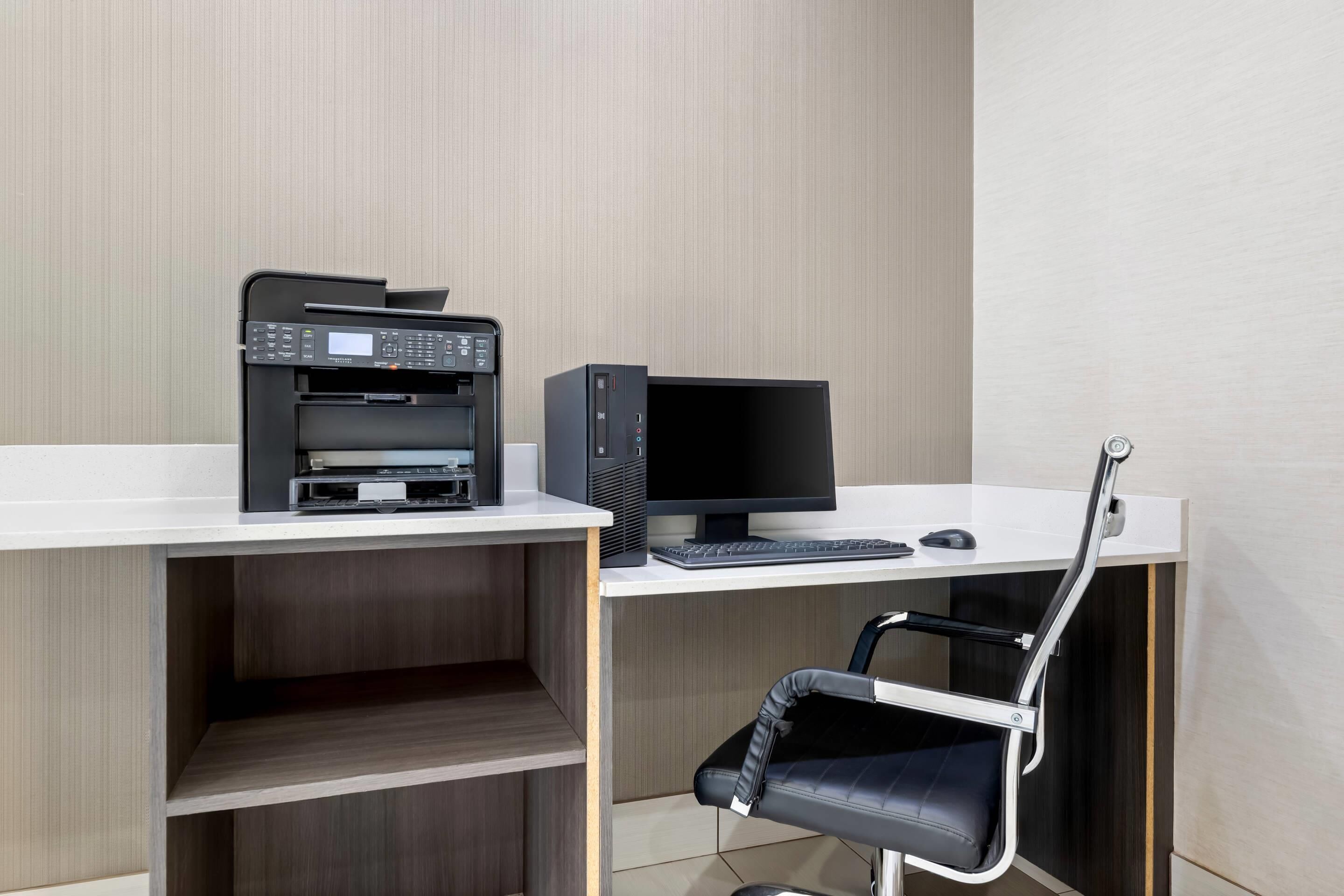 Een modern bureau met een printer, computer monitor, toetsenbord en stoel.