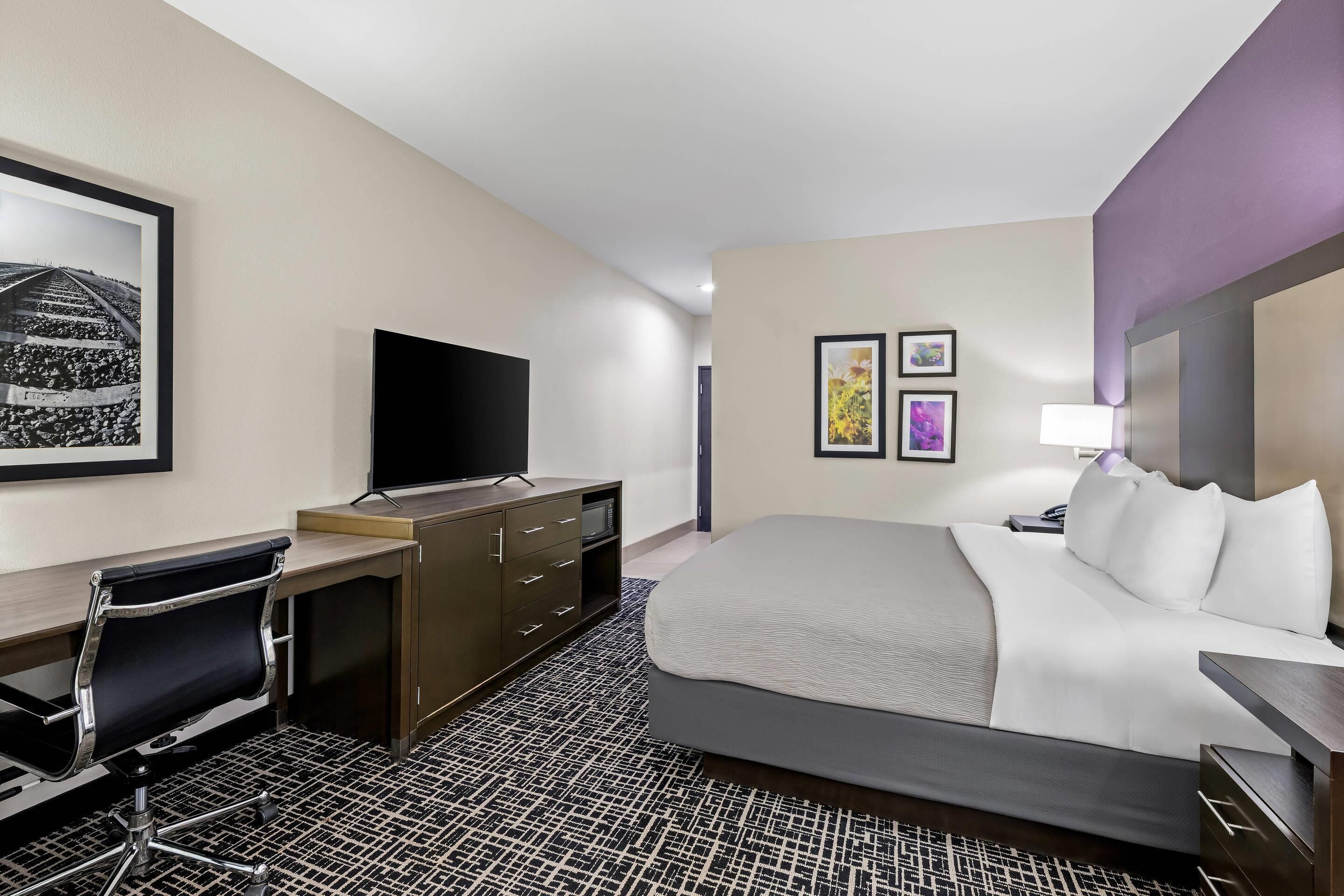 A hotel room with a bed, desk, chair, television, and artwork on the walls.
