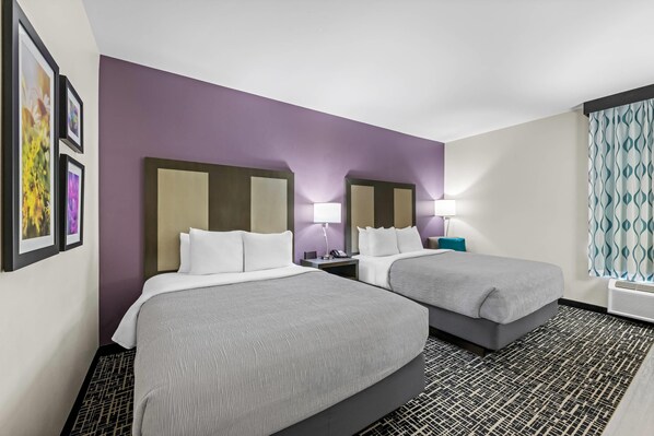 Habitación de hotel con dos camas, un tapete estampado, una pared de acento morada y una ventana con cortinas.