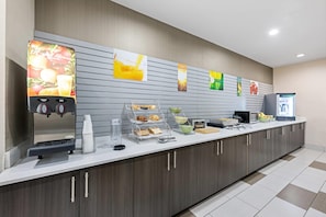 Een ontbijtbuffet met een koffieapparaat, een drankenspender en diverse soorten eten.