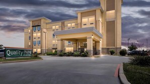 Un hôtel avec une enseigne indiquant « Quality INN & Suites », une entrée abritée et un parking.