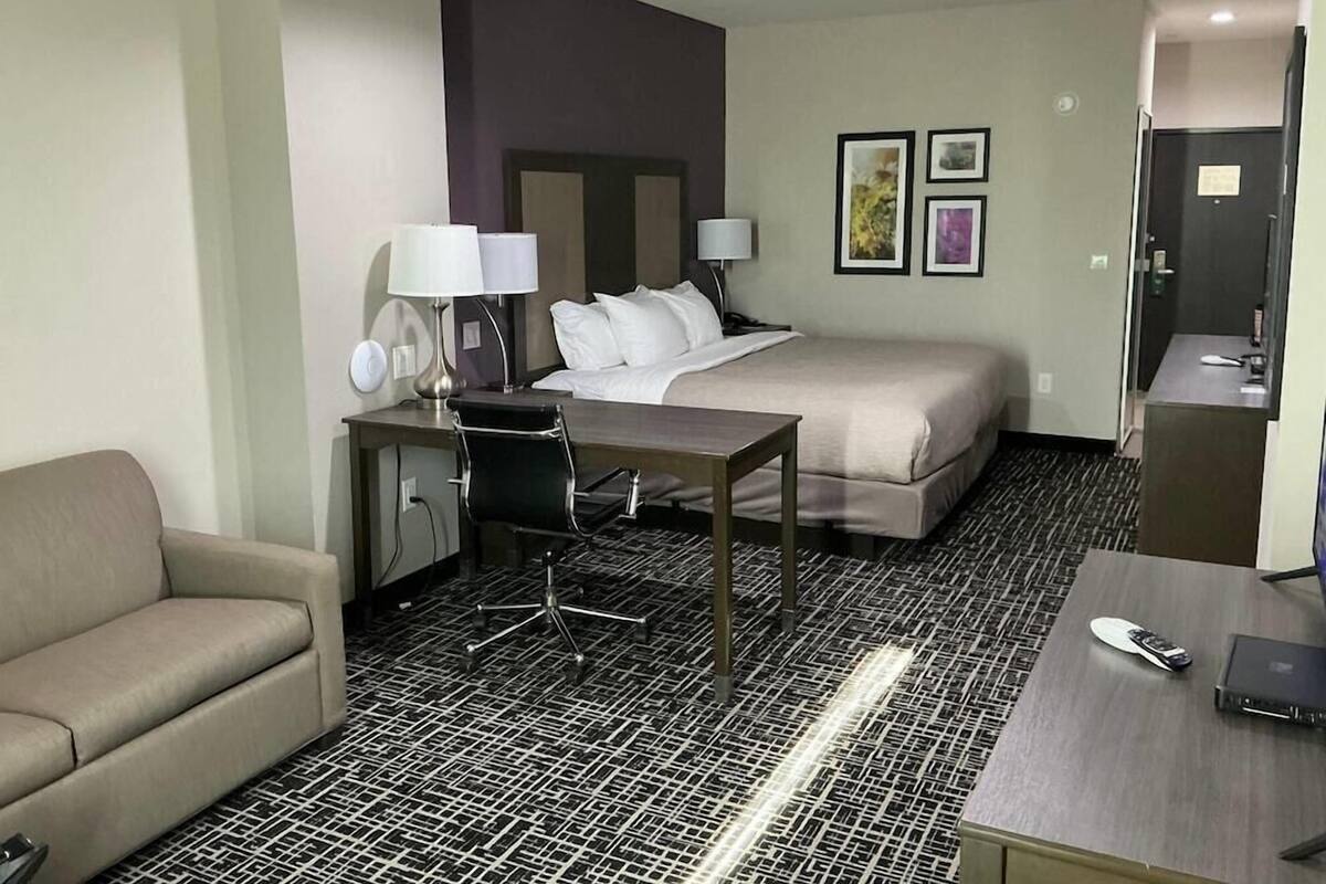 Een hotelkamer met een bed, een bureau met stoel, een bank en een kleine kitchenette.