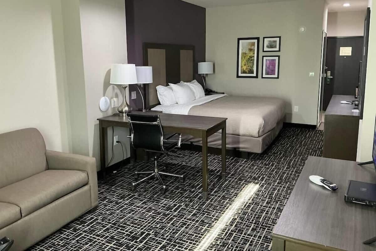 A hotel room with a bed, a desk with a chair, a sofa, and a small kitchenette.
