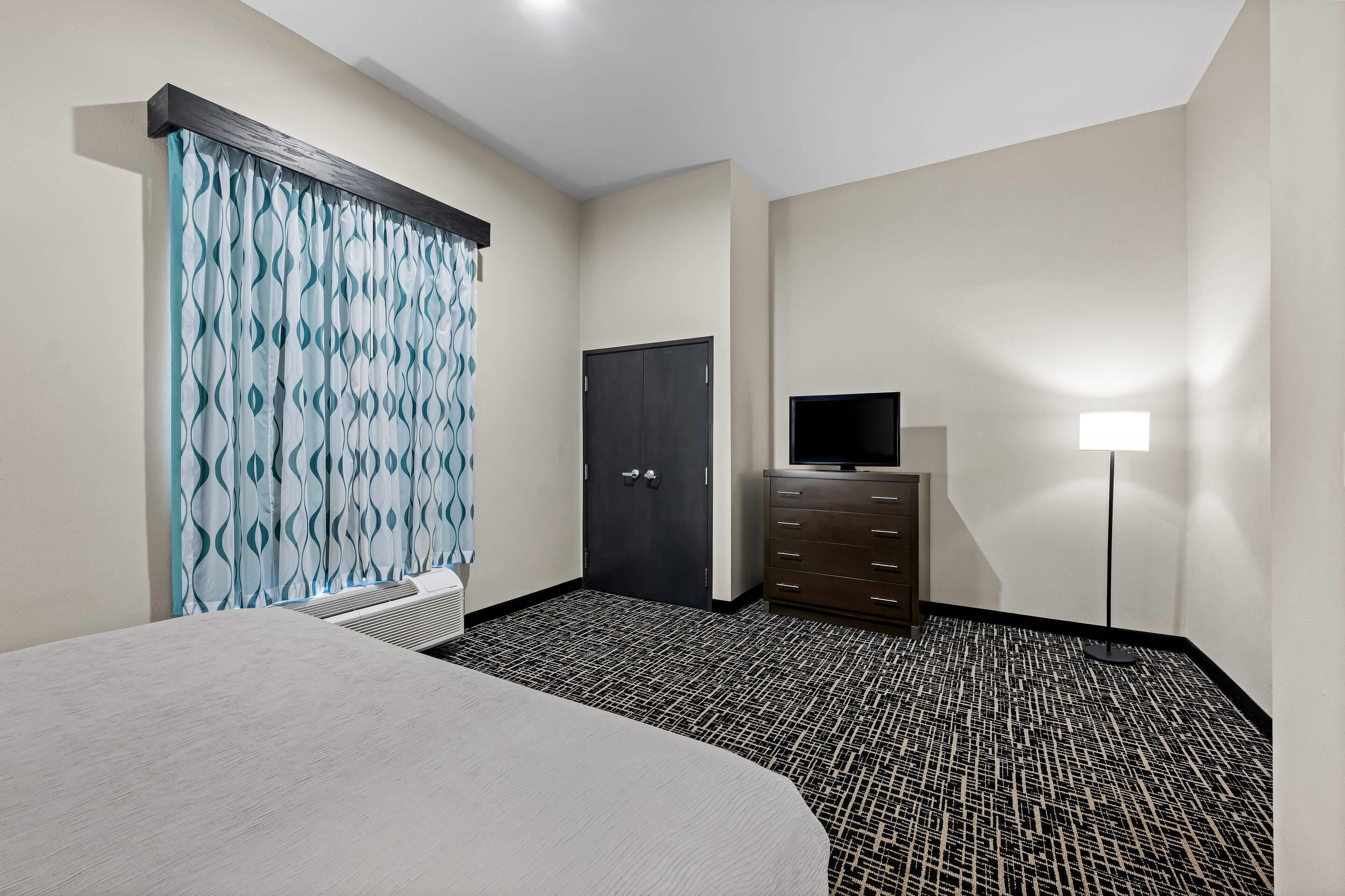 A hotel room with a bed, a dresser, a television, a desk, and a floor lamp.