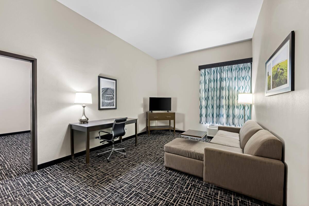 Een hotelkamer met een bureau, stoel, televisie, bank en een kamer met een patroon.