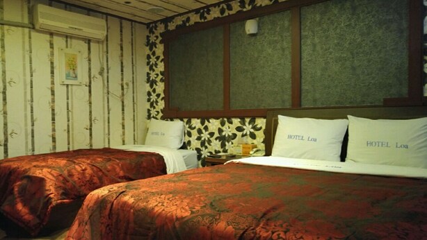 Una habitación con dos camas, cada una con cubrecama y almohadas estampadas con el nombre "HOTEL Loa". La habitación tiene techo de madera y paredes con un panel decorativo.