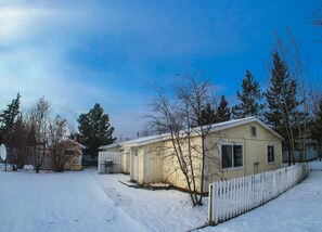 A single-story house with a white picket fence, a small porch, and a snow-covered yard.