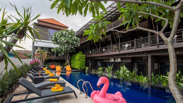 A pool area with lounge chairs, a pink flamingo float, and a building with balconies. - Hotel L'Amore Bali (Seminyak)