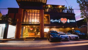 A hotel with a prominent heart-shaped sign, a Christmas tree, and several cars parked in front. - Hotel L'Amore Bali (Seminyak)
