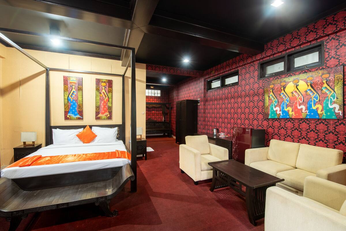 A hotel room with a large bed, a sofa, a coffee table, and artwork on the walls.