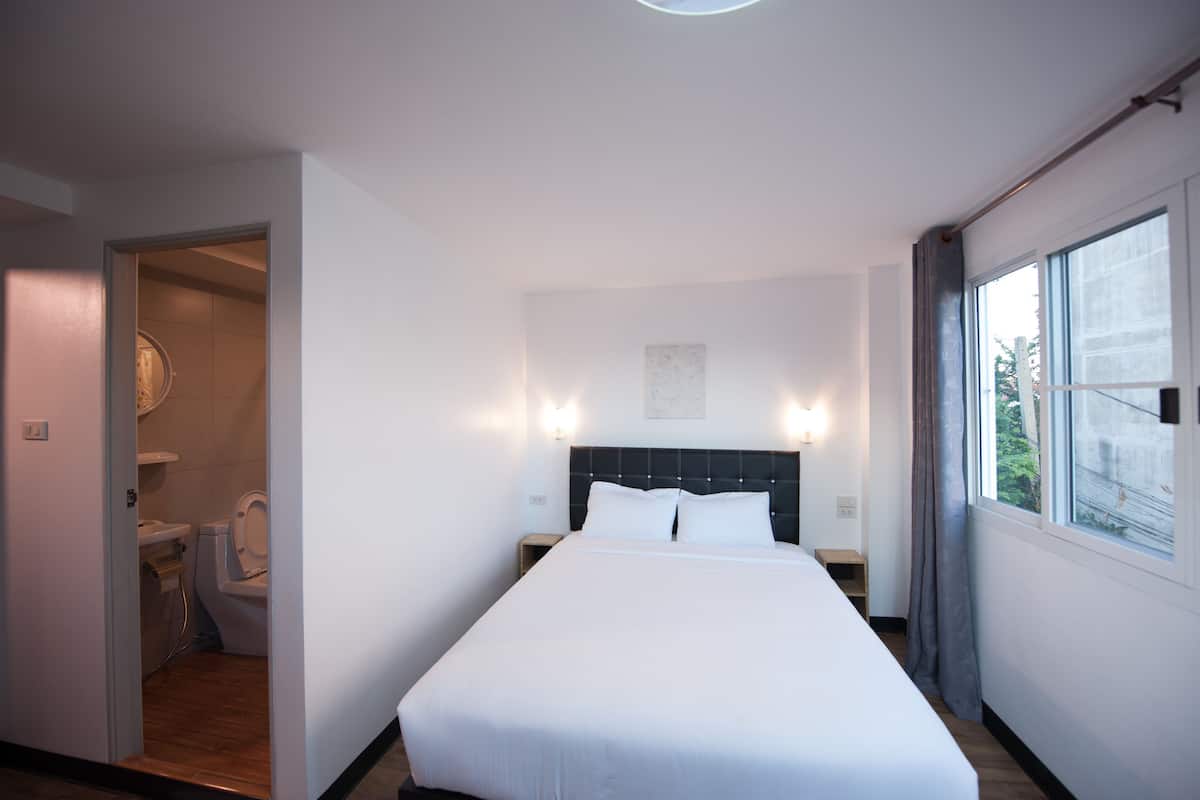A hotel room with a large bed, a window with curtains, a bedside table, and a view of the outdoors.