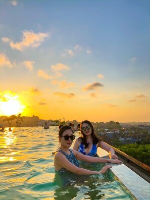 Two individuals in a swimming pool with a sunset view.