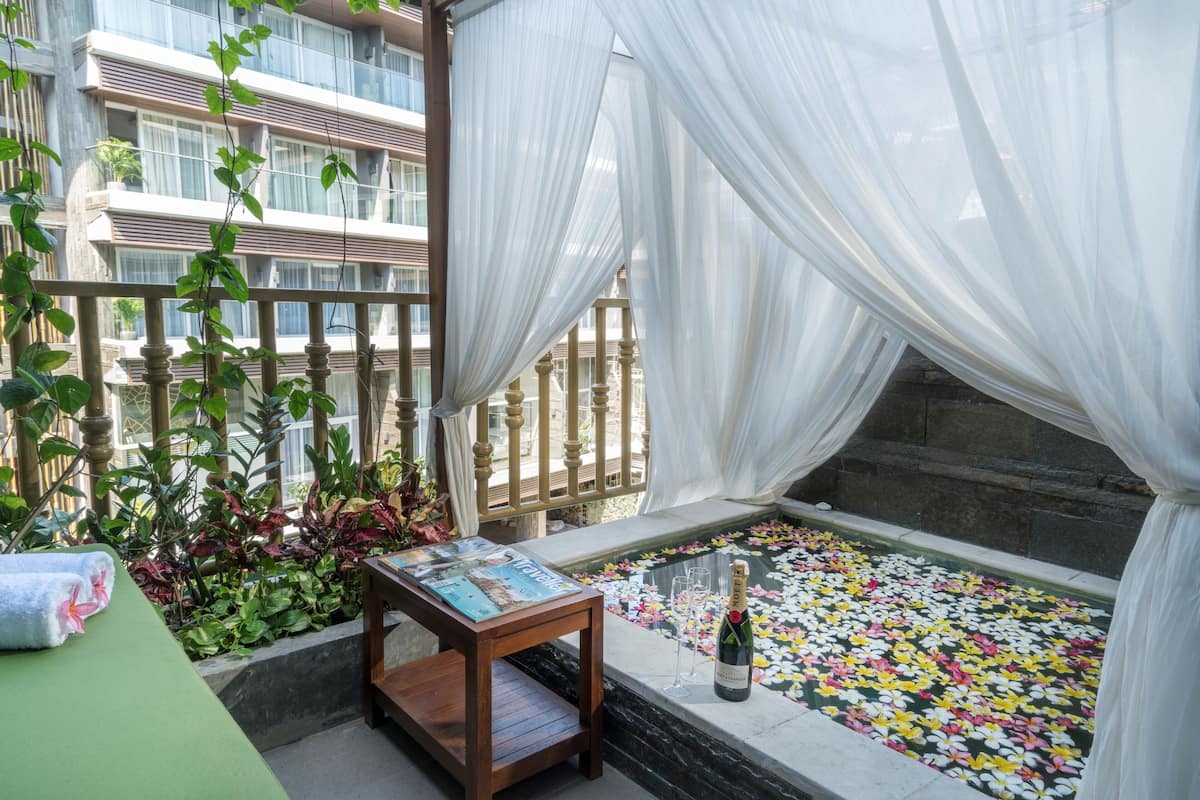 A balcony with a table, a bottle of champagne, and a flower-filled water feature.