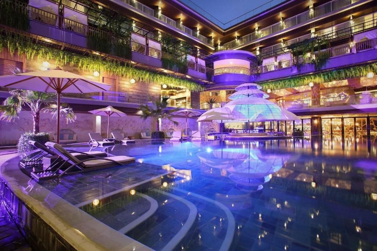 Ein mehrstöckiges Hotel mit einem zentral gelegenen Schwimmbad, Sitzgelegenheiten im Freien und üppiger Bepflanzung.