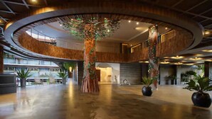 A spacious lobby with a central tree, wooden paneling, and potted plants. - The Crystal Luxury Bay Resort Nusa Dua (Nusa Dua)