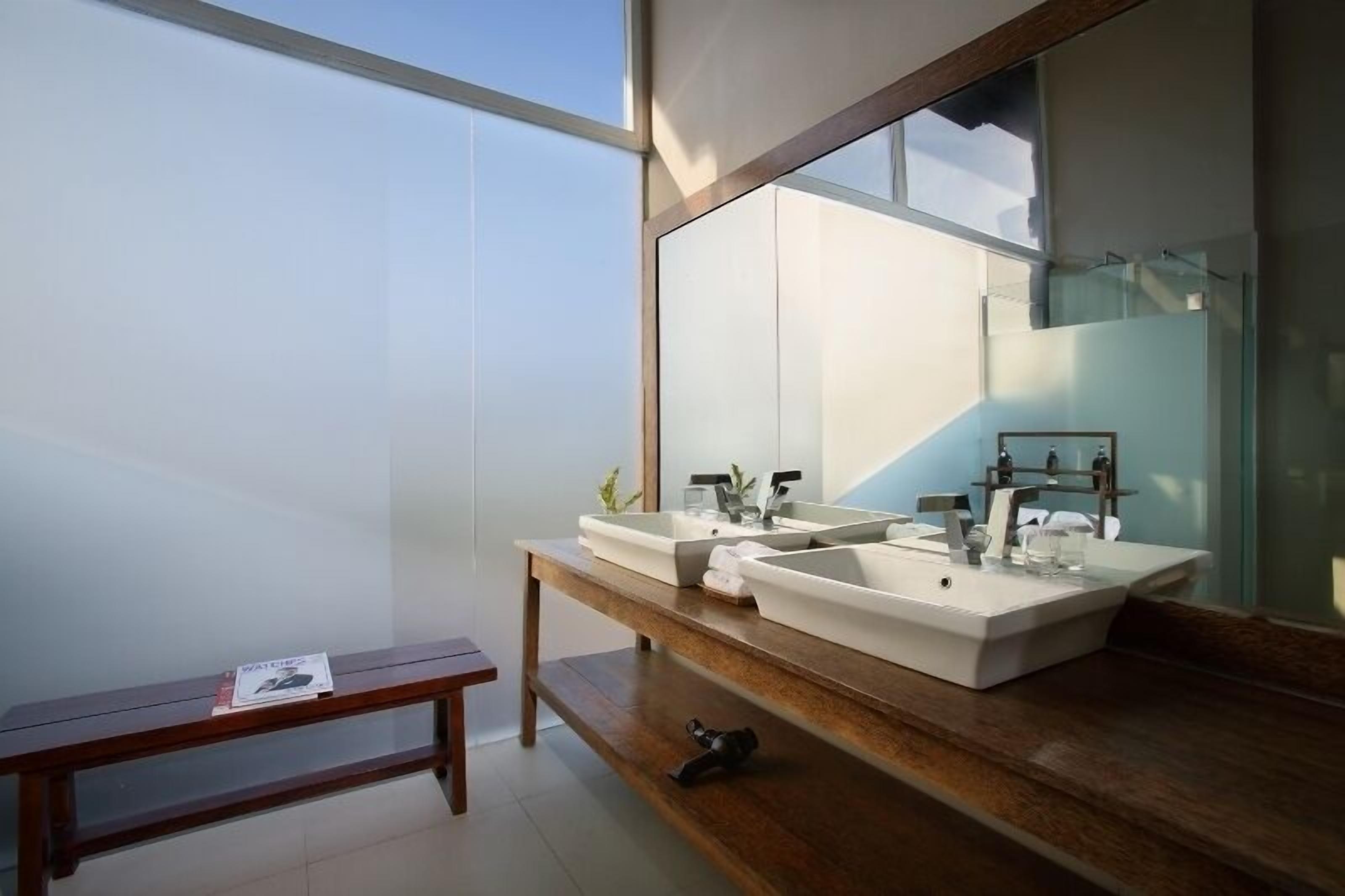 A modern bathroom with two large sinks, a mirror, and a bench.