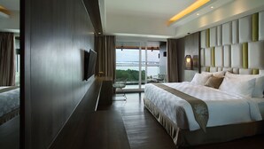 A modern hotel room with a large bed, a flat-screen TV, a seating area with a table and chairs, and a balcony with a view. - The Crystal Luxury Bay Resort Nusa Dua (Nusa Dua)