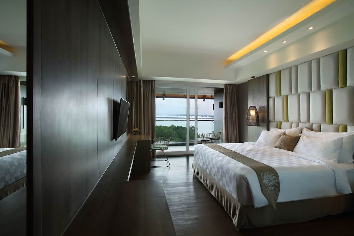A modern hotel room with a large bed, a flat-screen TV, a seating area with a table and chairs, and a view of the outdoors.