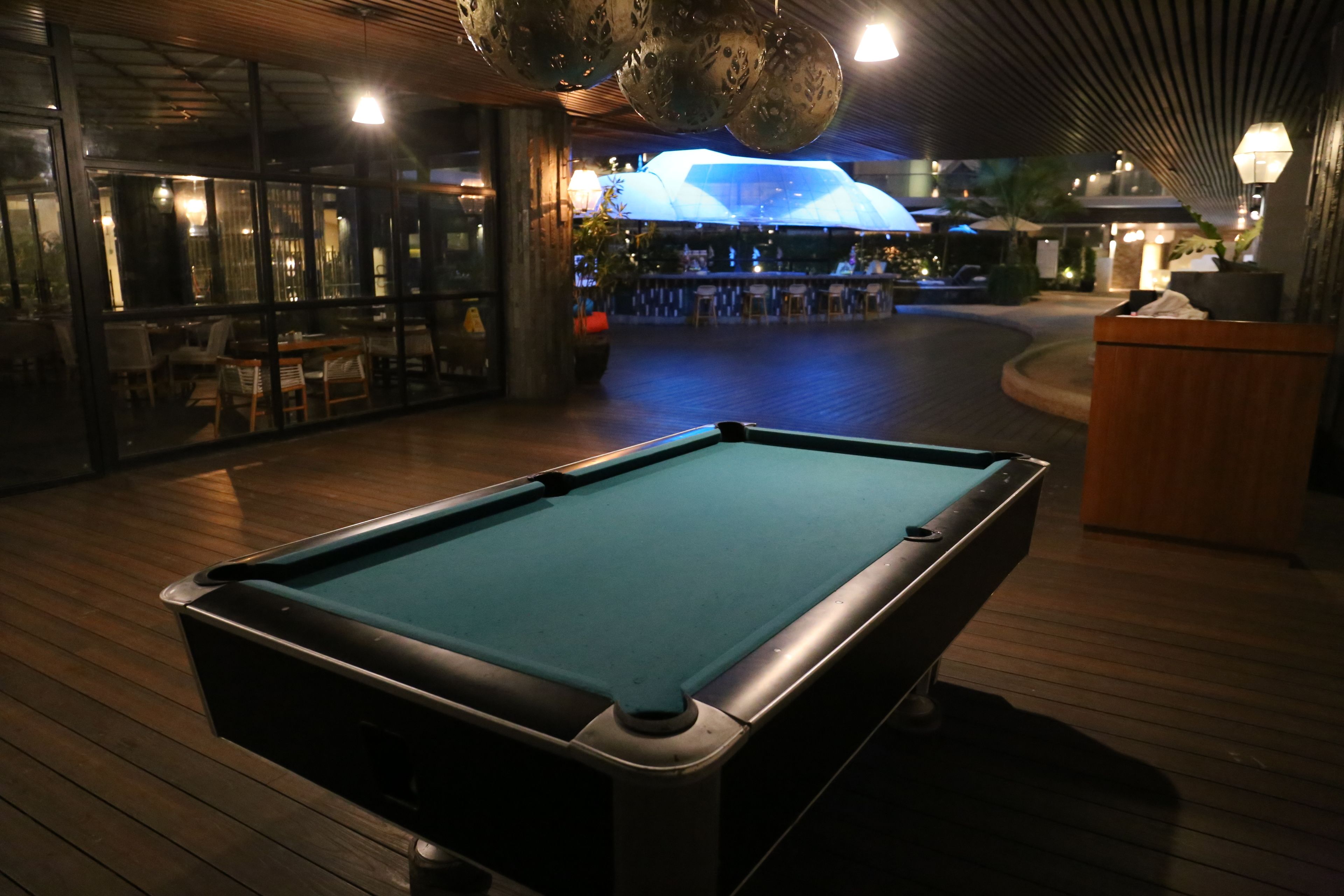A pool table in a dimly lit indoor area with a bar and seating in the background.
